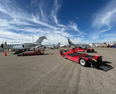 A busy airport tarmac featuring several private jets parked under a bright blue sky with wispy clouds